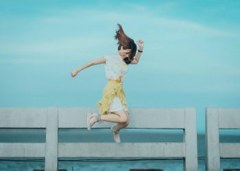 Jumpshot Photography of Woman in White and Yellow Dress Near Body of Water